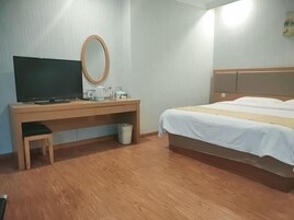 Habitación de hotel con escritorio de madera, televisor, espejo, cama con ropa blanca y un pequeño cubo de basura.