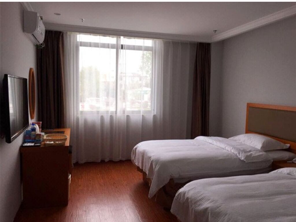 Habitación de hotel con dos camas, televisión, cómoda de madera y un ventanal con cortinas.