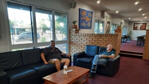 Two men seated on a black leather sofa and a wooden coffee table in a room with brick walls and large windows.