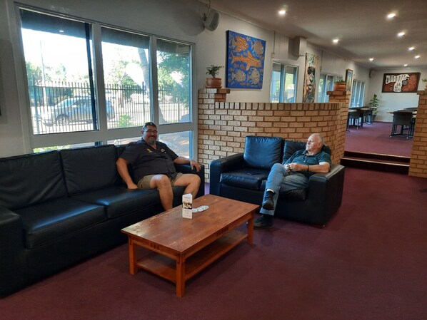 Two men seated on a black leather sofa and a wooden coffee table in a room with brick walls and large windows.