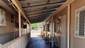 A covered outdoor area with a wooden deck, a railing, and a few chairs.