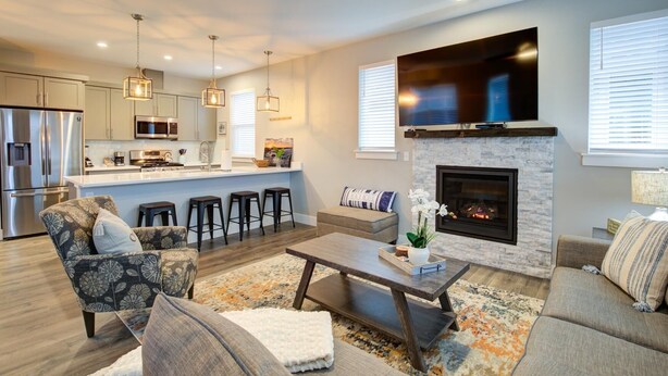 A modern living room with a fireplace, a kitchen with bar stools, and a large TV.