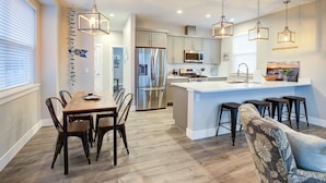 A modern kitchen with a central island, stainless steel appliances, pendant lighting, and a dining area with a wooden table and chairs.