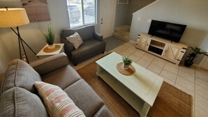 Una sala de estar con un sofá, una mesa de centro, un televisor y una escalera.