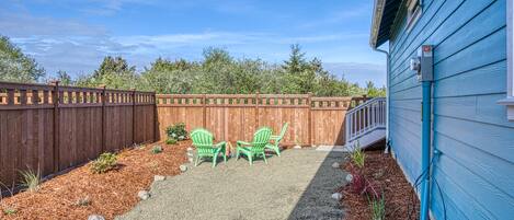 A backyard with a wooden fence, two green chairs, and a gravel path.