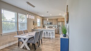 Una cucina moderna con elettrodomestici in acciaio inossidabile, un'area pranzo con tavolo bianco e sedie grigie, e un'ampia finestra con tende.