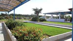 A covered outdoor area with a pathway, a flower bed, and a grassy field. - Gran Torre Hotel (Cabras)