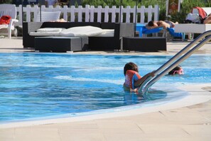 Una piscina con sillones de descanso y una cerca blanca en el fondo.