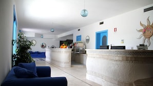 A reception area with a blue sofa, a reception desk, a large mirror, and a decorative sun wall. - Gran Torre Hotel (Cabras)