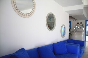 Una sala de estar con un sofá azul, dos espejos en la pared y un espejo decorativo sobre un aparador.
