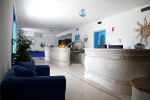 Zona de recepción con sofá azul, mostrador de recepción, un espejo grande y un panel decorativo con motivos solares.