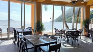 A restaurant with large windows overlooking a beach and ocean, featuring tables and chairs arranged for dining. - Siam Royal View Resort Apartments (Koh Chang)