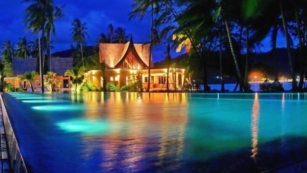 A resort with a swimming pool, palm trees, and a building with a thatched roof. - Siam Royal View Resort Apartments (Koh Chang)