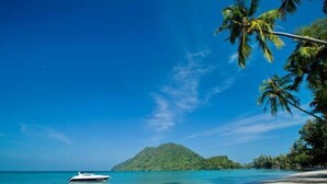 A beach with a boat, clear blue sky, and a small island in the distance. - Siam Royal View Resort Apartments (Koh Chang)