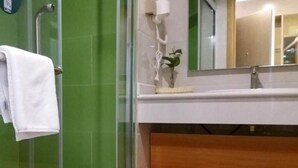 Ett badrum med en duschavdelning med glasväggar, en vit handduk hängande på en hylla, en spegel ovanför en trähylla och en grön kakelbeklädd vägg.