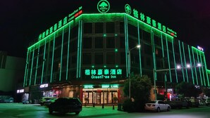 A hotel with a prominent Green Tree Inn sign, featuring a large entrance and a modern facade with vertical lighting accents. - Greentree Inn Bozhou Lixin District Huishang Market (Bozhou)