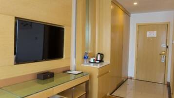 A hotel room with a glass desk, a flat-screen TV, a coffee maker, and a door with a sign.