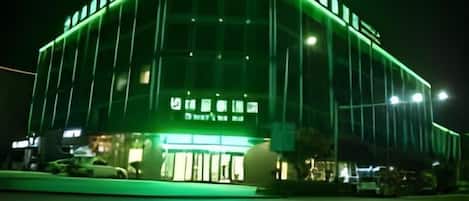 Un edificio con fachada iluminada en verde y un logotipo circular en la parte superior.