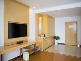 Habitación de hotel con un mueble bajo de madera para el televisor, una mesita con un hervidor, un cesto de basura y una planta en maceta.