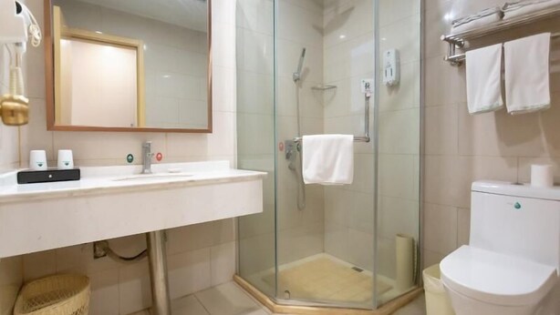 Un baño moderno con ducha de vidrio, un lavabo blanco con espejo y un inodoro con toallero.