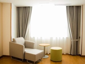 A hotel room with a single sofa, a small round table, and a green ottoman. - Greentree Inn Bozhou Lixin District Huishang Market (Bozhou)