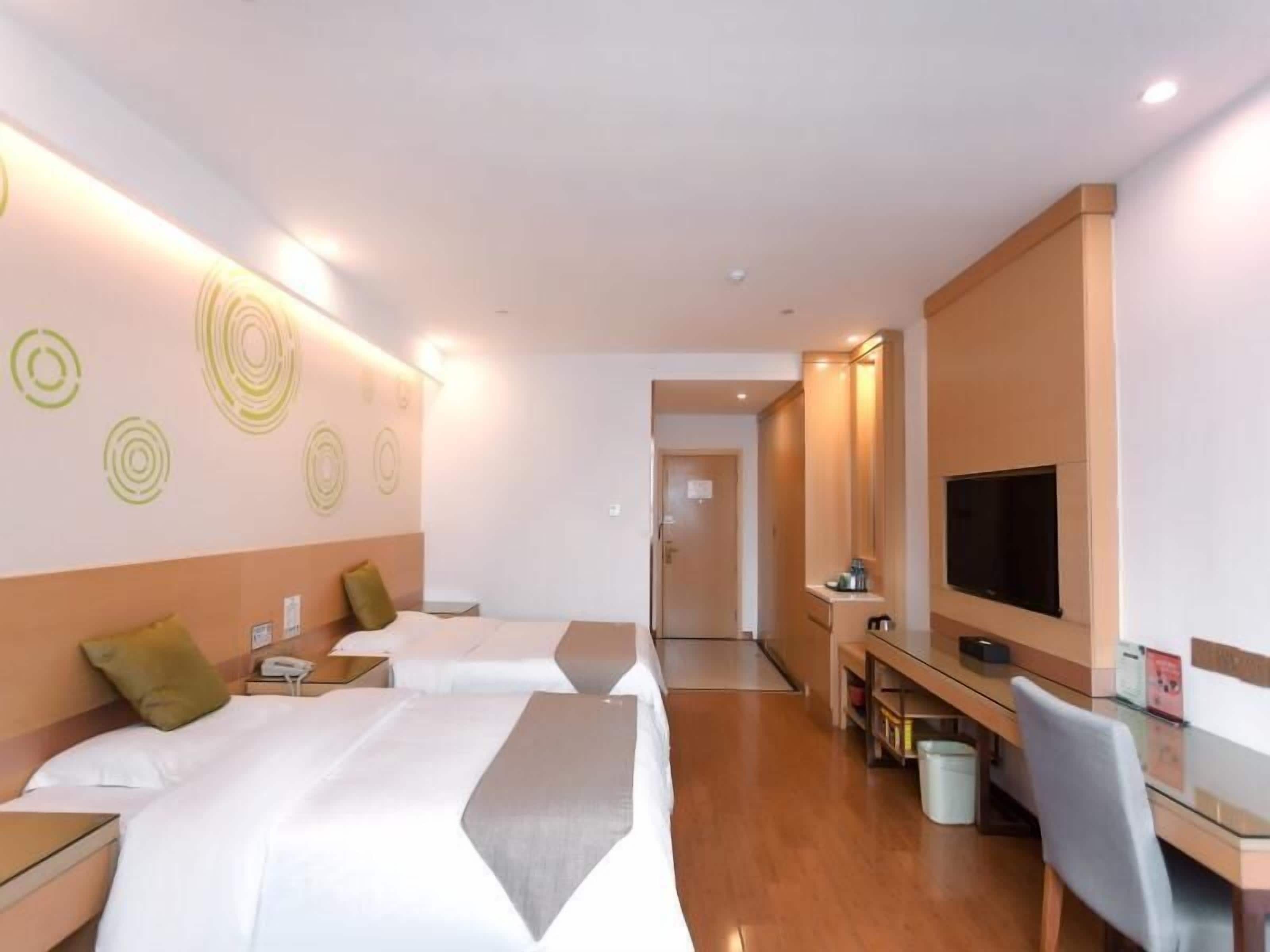 A hotel room with two beds, a desk with a TV, and a bathroom in the background.
