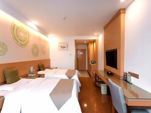 Habitación de hotel con dos camas, un escritorio, un televisor y un baño visible a través de una puerta abierta.