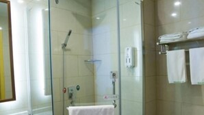 Cabina de ducha con paredes de vidrio, una toalla blanca colgada en un perchero, un inodoro y un lavabo con un espejo arriba.