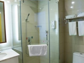 Cabina de ducha con paredes de vidrio, una toalla blanca colgada en un perchero, un inodoro y un lavabo con un espejo arriba.