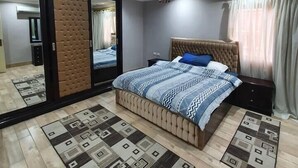 A bedroom with a large bed, a mirror, a wardrobe, and a ceiling light. - Charming 3-Bed Apartment in New Cairo City (New Cairo City)