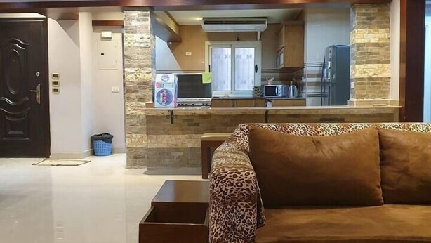 A modern living room with a sofa, a coffee table, and a kitchen area in the background. - Charming 3-Bed Apartment in New Cairo City (New Cairo City)
