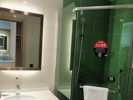 Un baño con ducha acristalada, lavamanos con espejo y toalla colgada en un perchero.