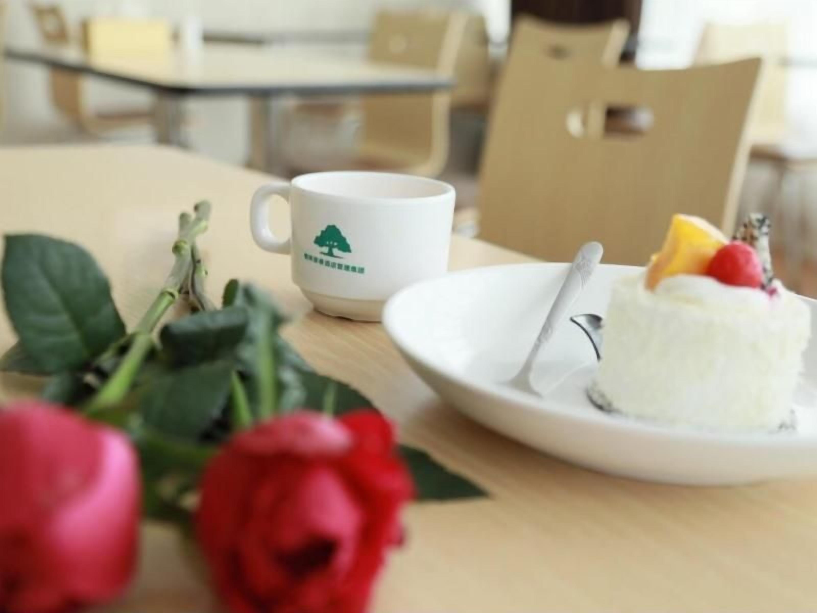 Una mesa de comedor con un plato blanco que sostiene un postre, una taza blanca con un logo de árbol y una rosa roja.