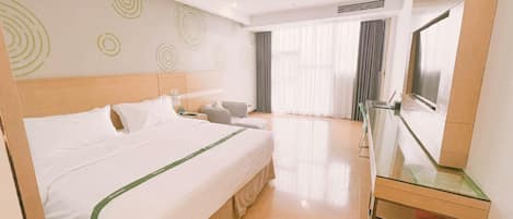 Habitación de hotel con una cama grande, un escritorio, una silla, televisión y ventana con cortinas.