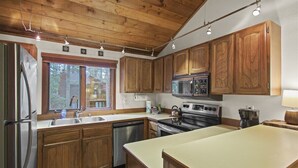 Una cocina con armarios de madera, electrodomésticos de acero inoxidable, una isla grande y un ventanal con vistas a una cabaña.