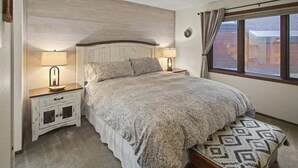 Un dormitorio con una cama, dos mesitas de noche con lámparas, una ventana con cortinas y un cabecero.