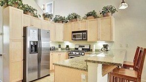 Une cuisine dotée de meubles en bois, d’un réfrigérateur en acier inoxydable, d’un four à micro-ondes, d’une cuisinière et d’un îlot central avec un comptoir en granit.
