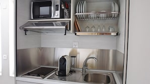 Eine kleine Küchenzeile mit Mikrowelle, Toaster und Geschirrgestell mit Tellern und Gläsern.