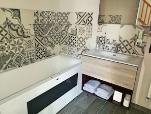 Un baño con bañera, lavamanos y tocador con toallas.
