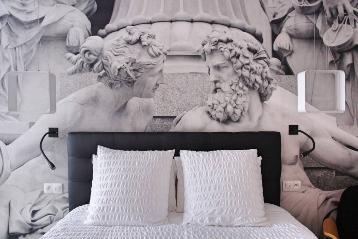 Una cama con ropa de cama blanca y un cabecero, frente a un mural grande y detallado.