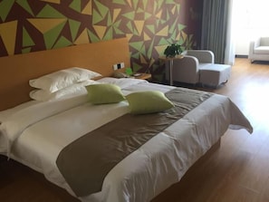 Ett hotellrum med en stor säng, två gröna kuddar, en sänggavel i trä och en vägg med ett geometriskt mönster.