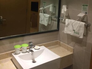 Un baño de hotel con lavamanos, espejo, toallero y artículos de aseo.
