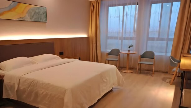 Una habitación de hotel con una cama grande, una mesita redonda pequeña con dos sillas y una ventana con cortinas.