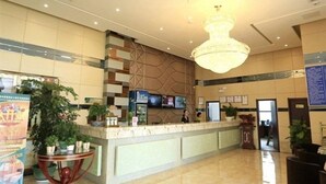 Un vestíbulo de hotel con un mostrador de recepción, una lámpara de araña grande y plantas en macetas.