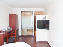 Quarto de hotel com uma cama, uma escrivaninha com cadeira, televisão na parede e uma porta de correr para o banheiro.
