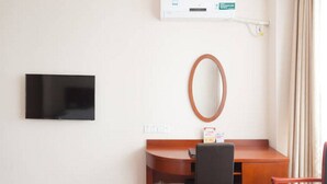 Habitación de hotel con televisor de pantalla plana en la pared, un escritorio de madera con silla, un espejo redondo y una mesita con una caja encima.