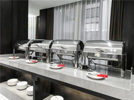 A buffet setup with three stainless steel dispensers, white plates, and red napkins.