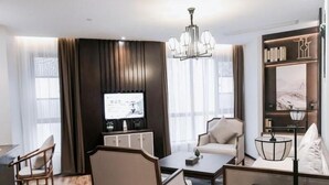A modern hotel room with a flat-screen TV, a sofa, a coffee table, and a bookshelf. - Greentree Eastern Yingtan City Guixi Municipal Government Hotel (Yingtan)