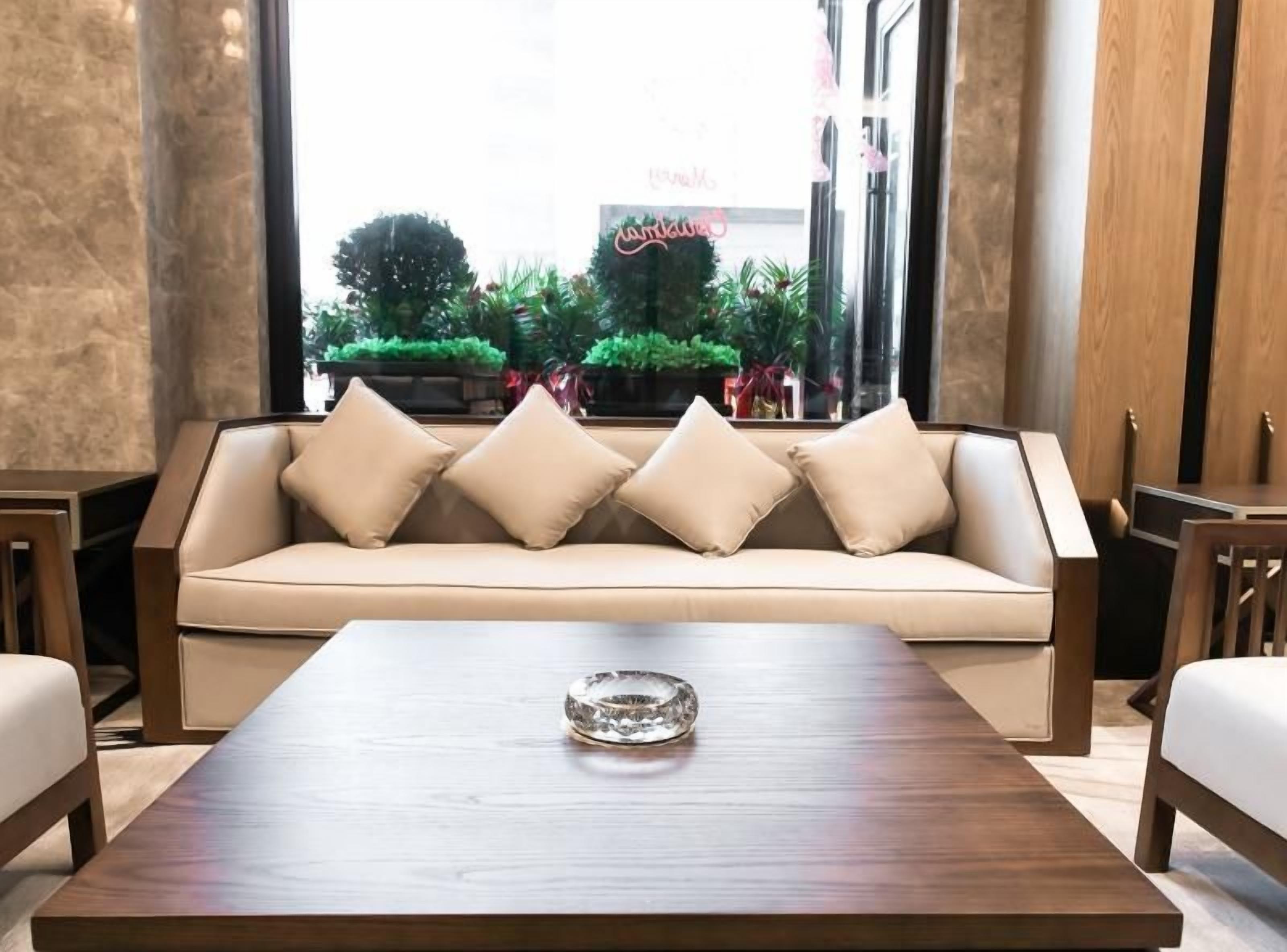A modern lounge area with a sofa, a wooden coffee table, and a view of a green outdoor space with plants and a neon sign.