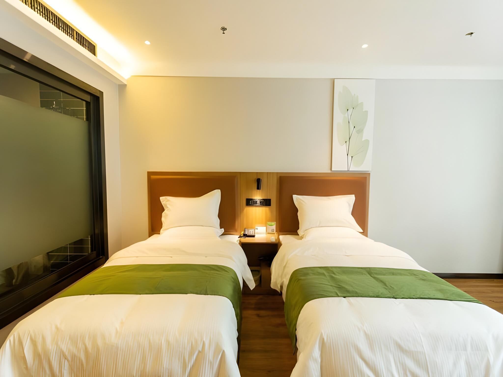 Habitación de hotel con dos camas, un espejo grande, una mesita de noche con lámpara y una obra de arte colgada en la pared.